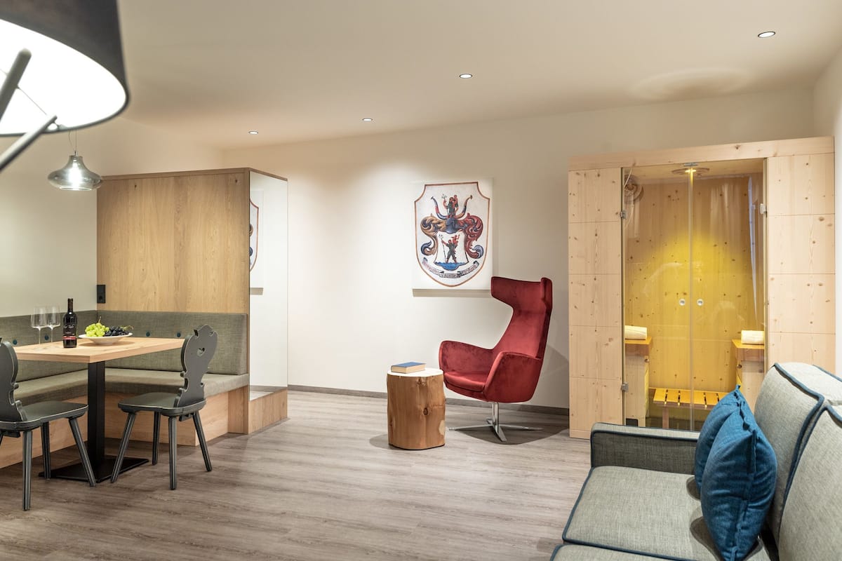 Un espace repas moderne avec une table en bois, des chaises et un banc. On y trouve une chaise rouge et un meuble en bois doté d’une porte en verre. Un porte-manteau avec un vêtement bleu est visible.