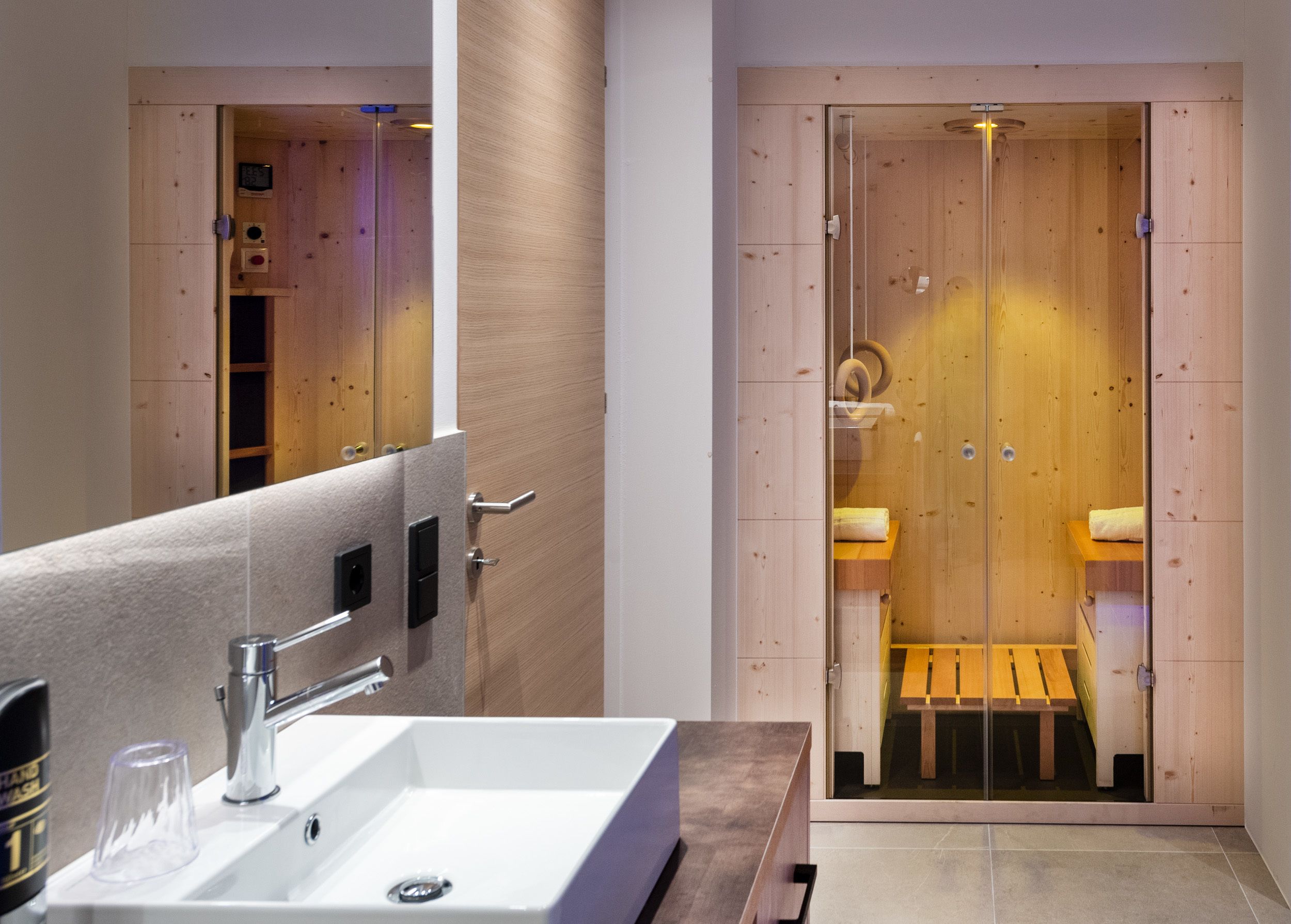 A modern bathroom with a large mirror, a sink, and a wooden shower enclosure.