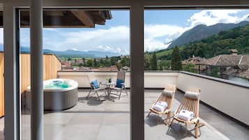 A balcony with a hot tub, two lounge chairs, and a table with chairs.