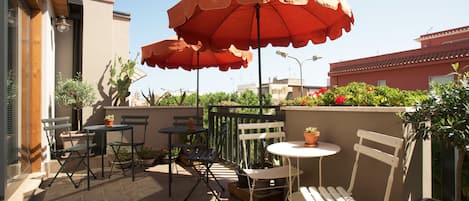 Une terrasse extérieure avec deux tables, quatre chaises et deux grands parasols.