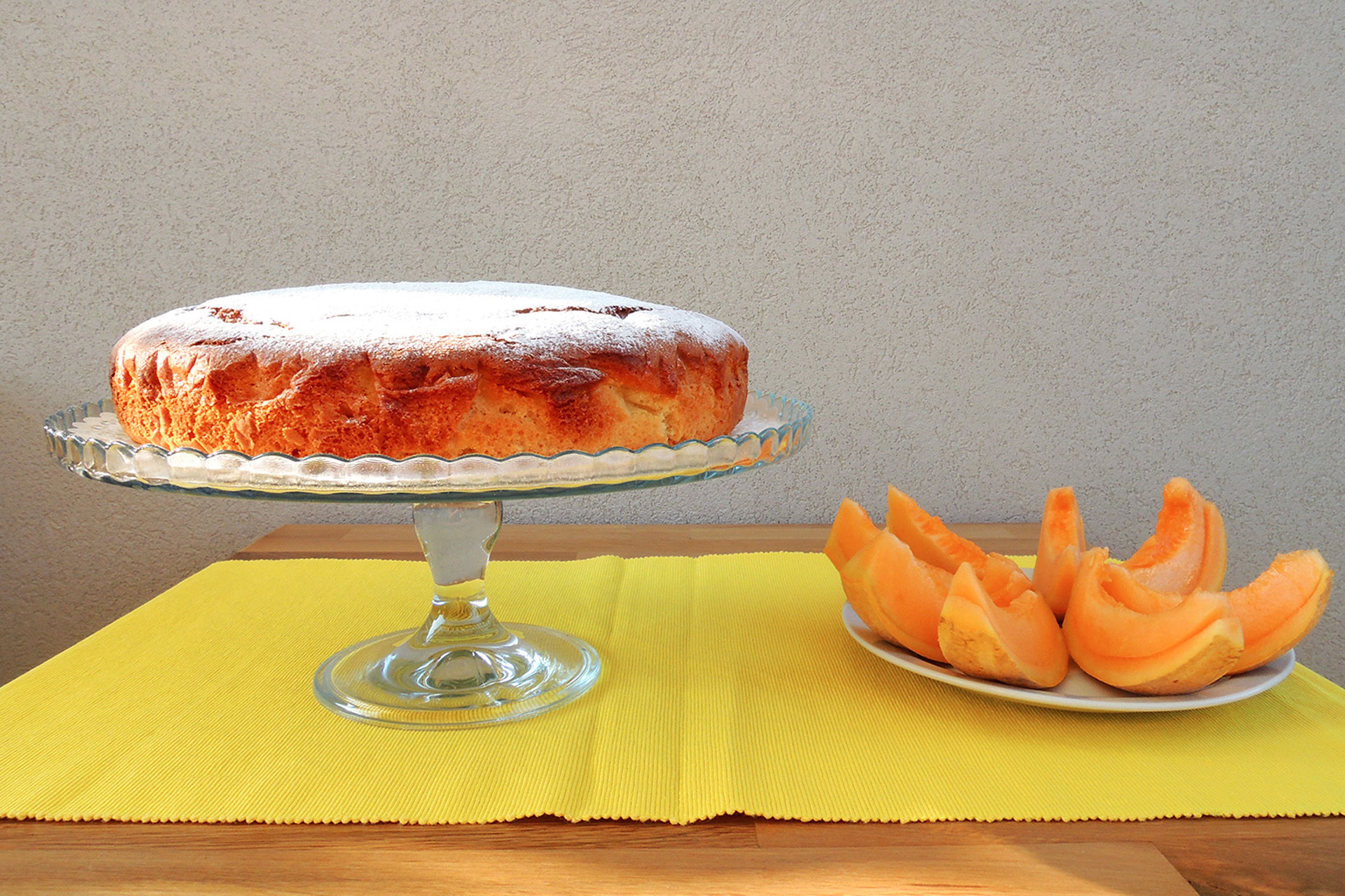 A round cake on a glass stand with a yellow placemat underneath.