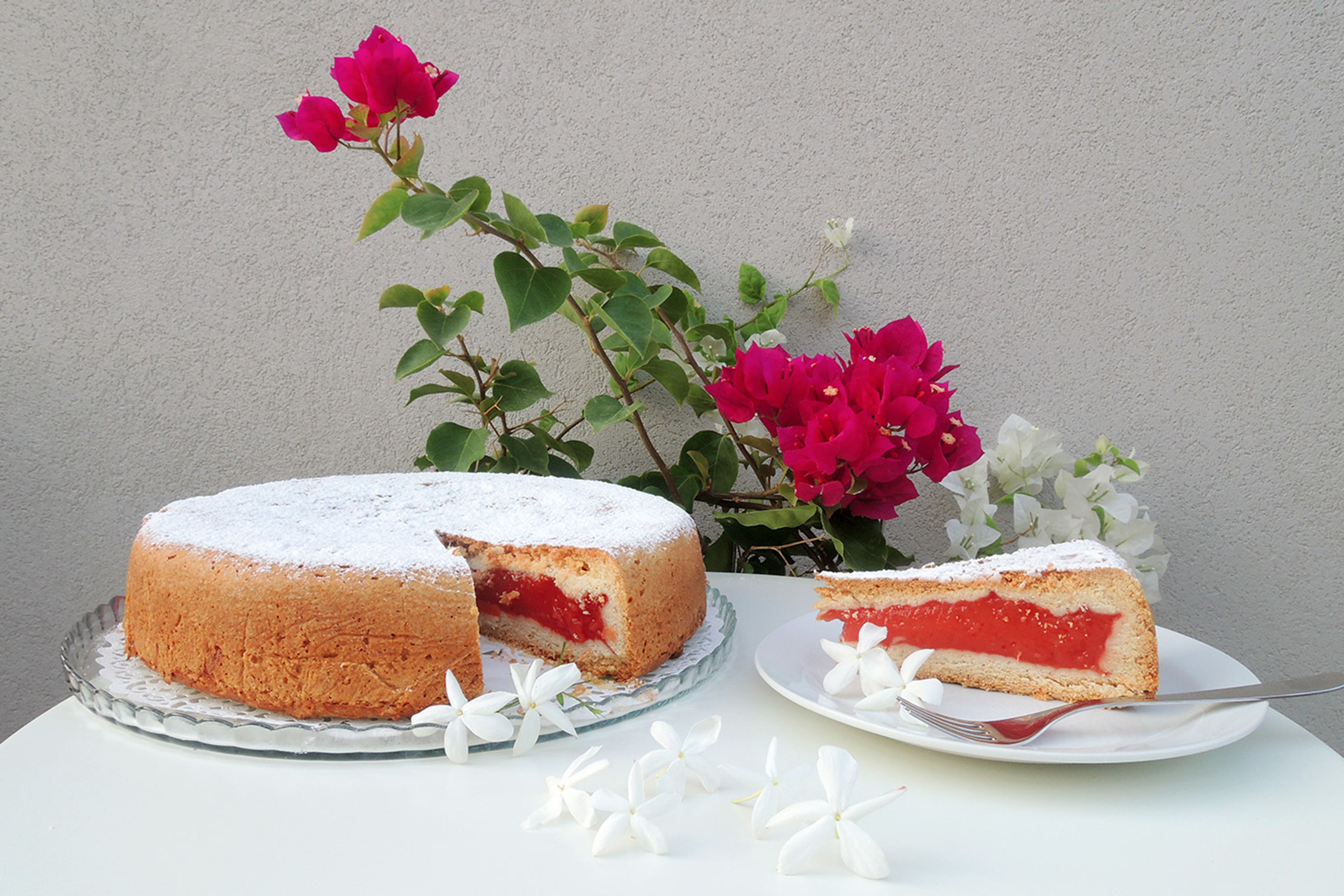 A round cake with a slice cut out, dusted with powdered sugar, and a slice on a plate beside it.