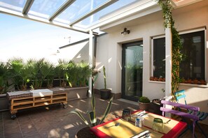Un patio con una mesa lista para comer, un carro de madera con toallas, plantas en macetas y una silla.