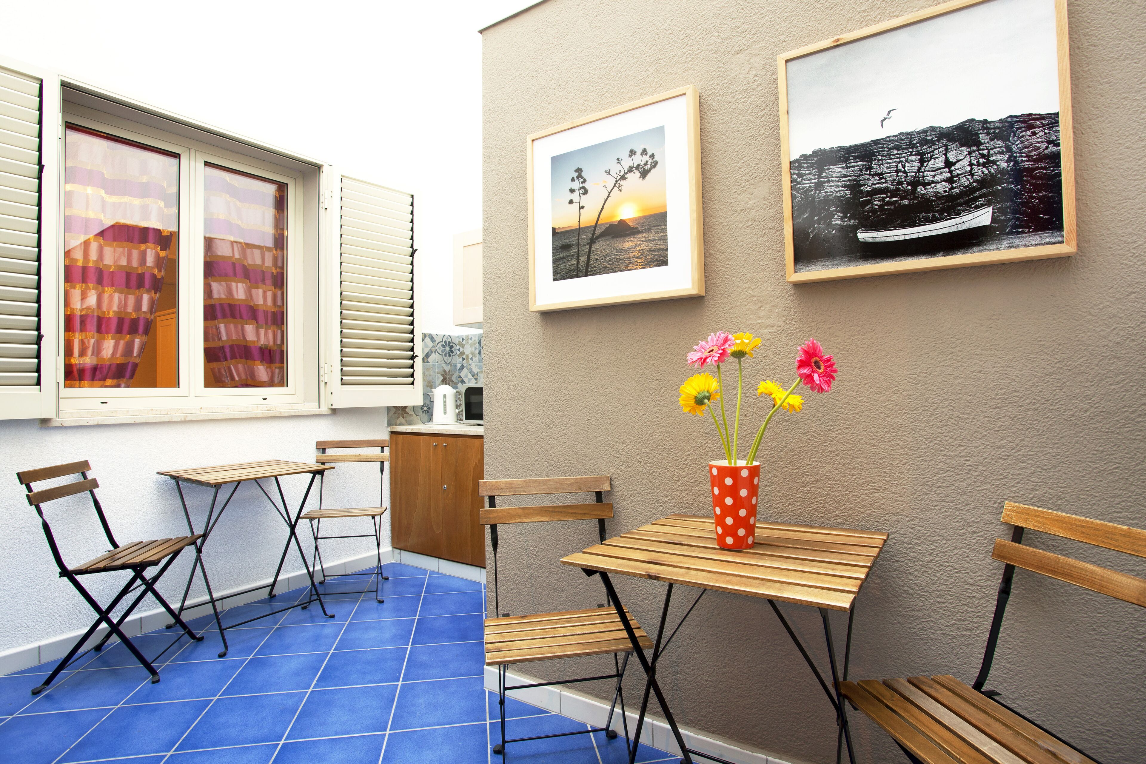 A small patio with blue tiles, wooden furniture, and two framed pictures on the wall.