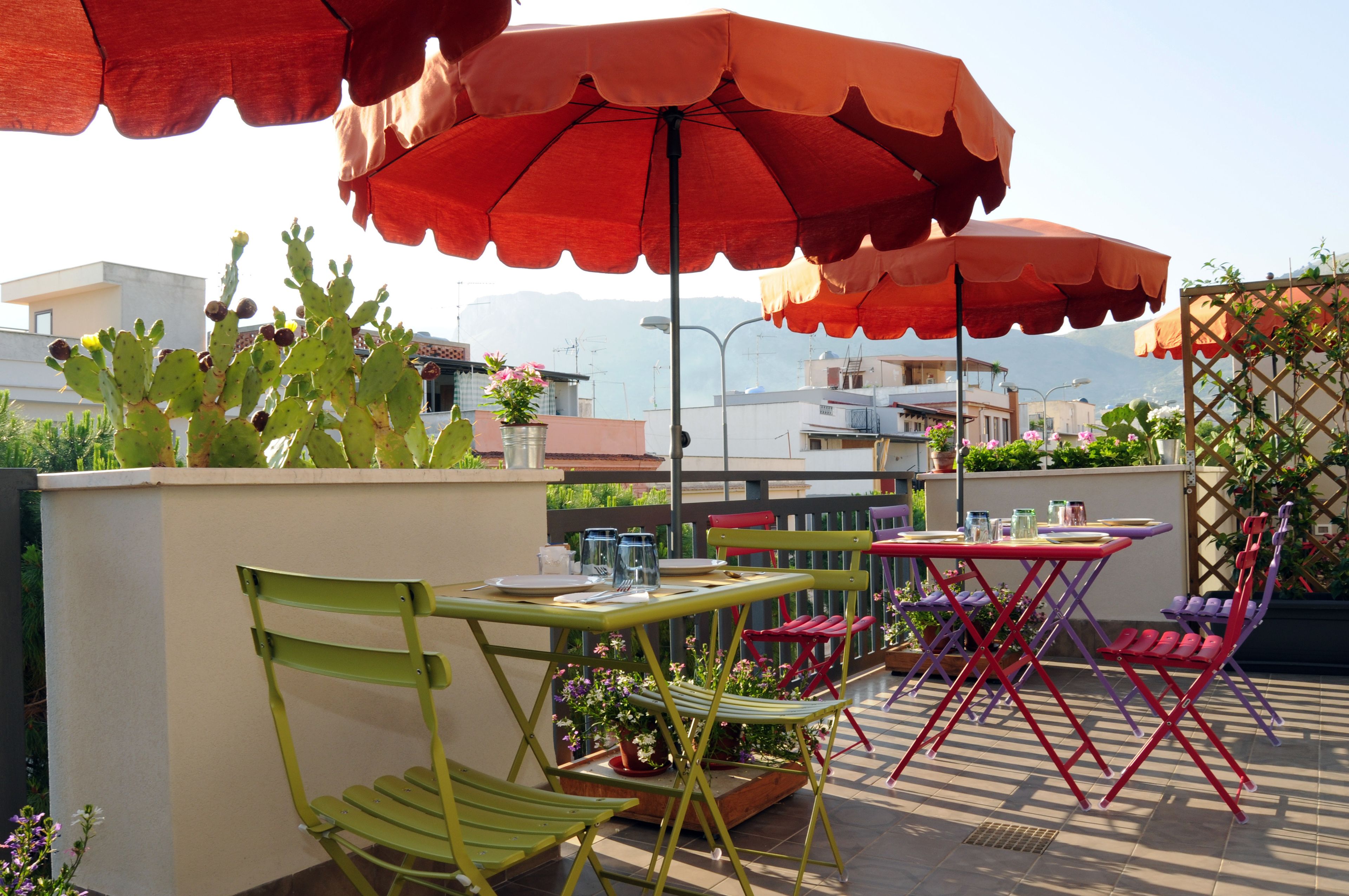 An outdoor patio with red umbrellas, green and red chairs, and a cactus plant.