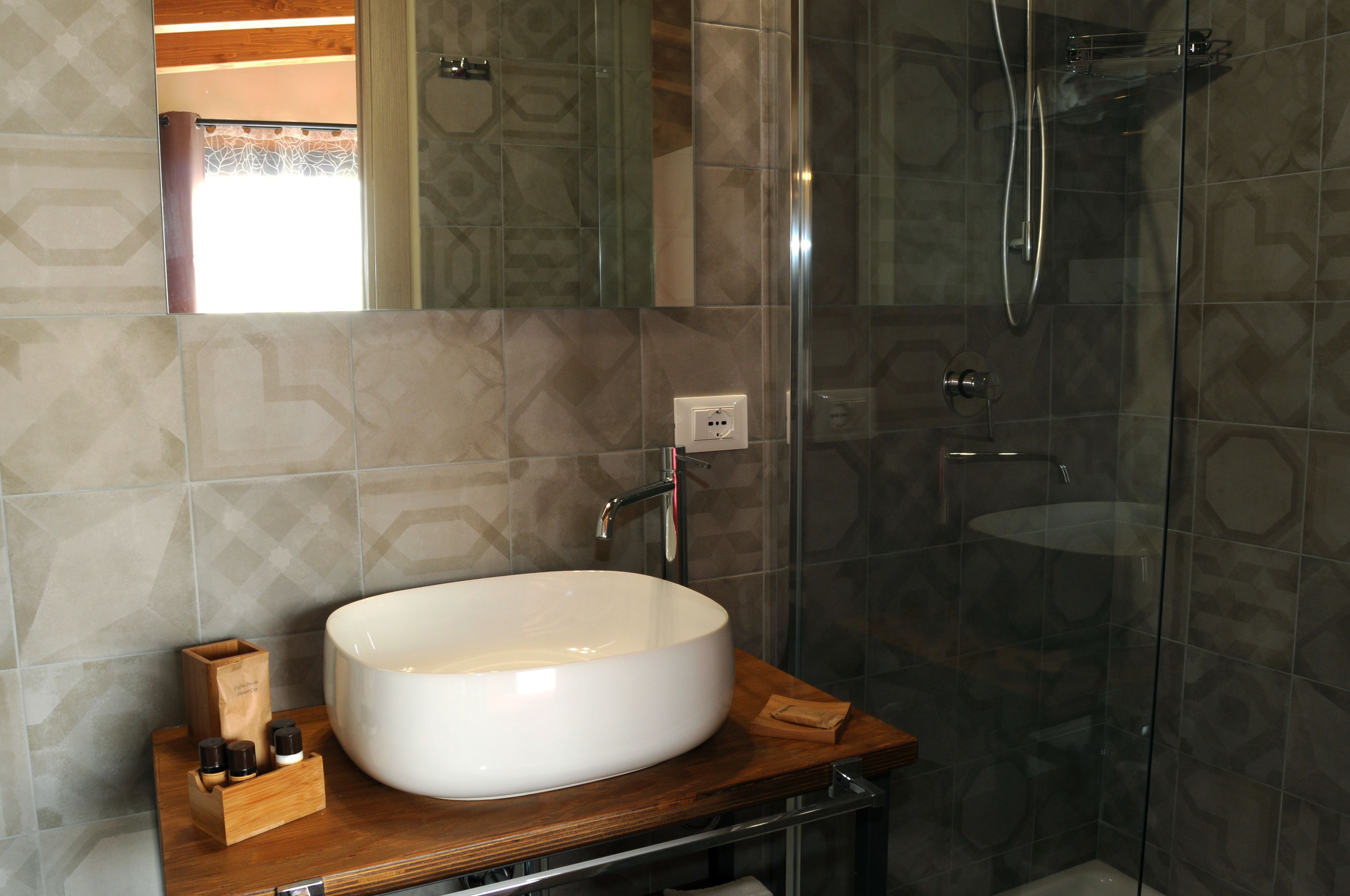 A modern bathroom with a large white sink, a wooden countertop, and a glass-enclosed shower.