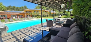 Un área junto a la piscina con sillones de descanso, una mesa y una pérgola.