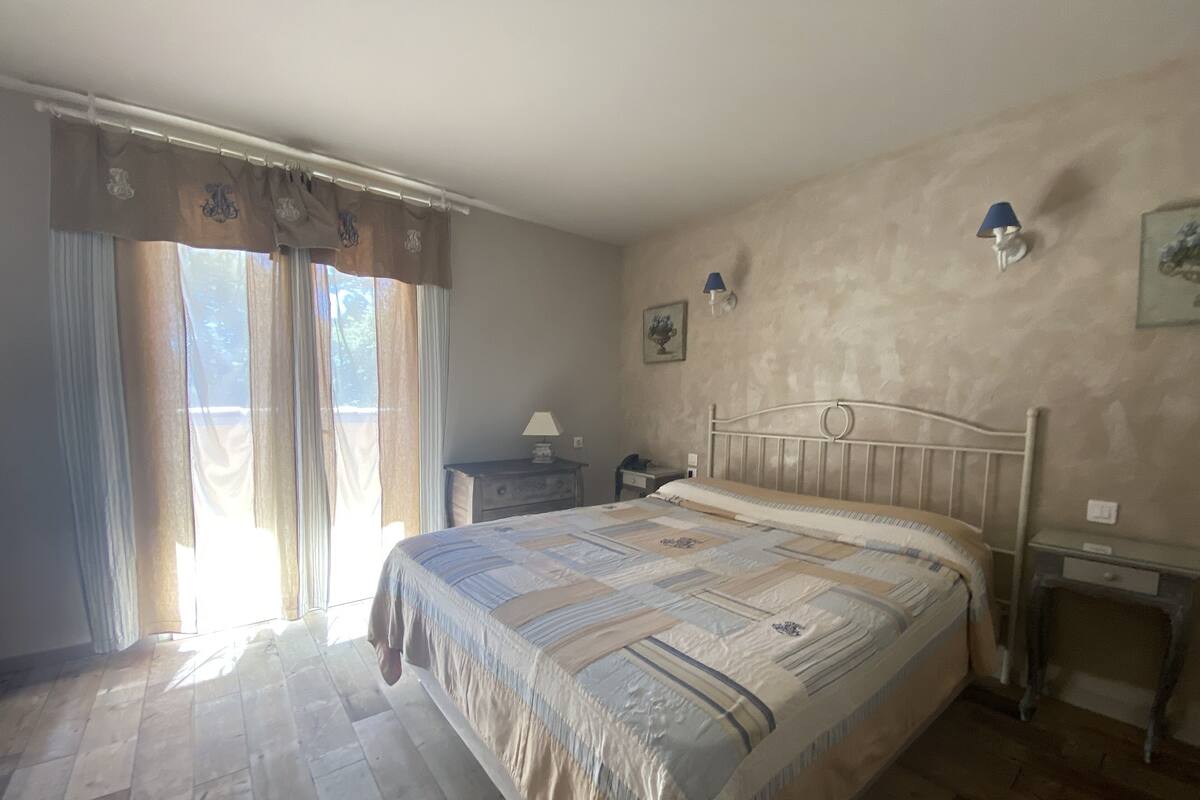 A bedroom with a bed, a nightstand, a lamp, and a window with curtains.