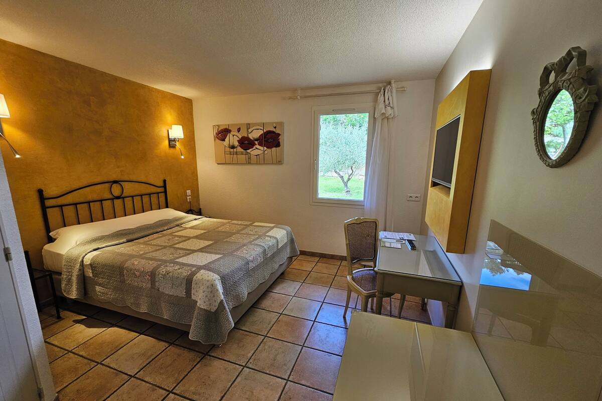 A bedroom with a bed, a desk, a chair, a window, and a painting on the wall.