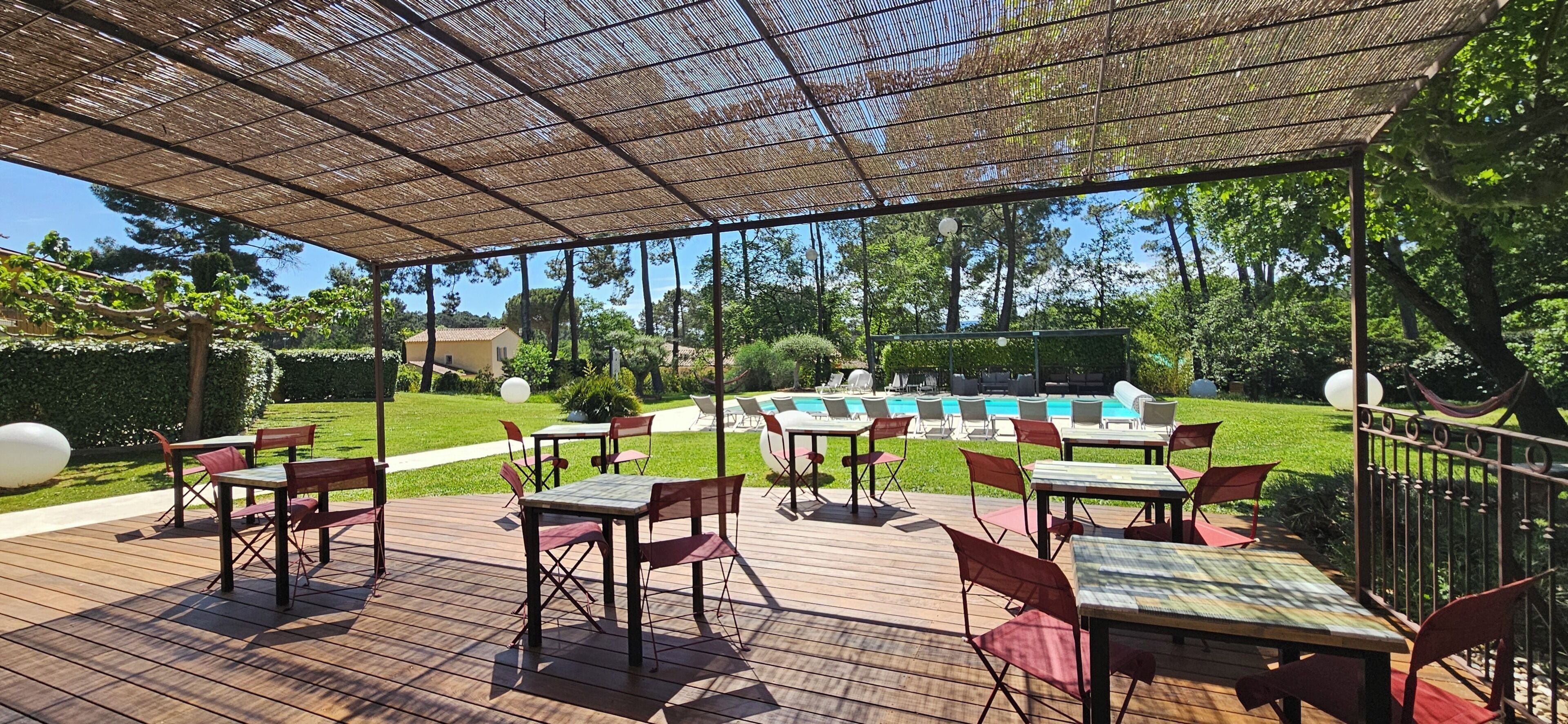An outdoor patio with tables and chairs, a pool, and a view of the surrounding greenery.