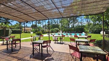 An outdoor patio with tables and chairs, a pool, and a view of the surrounding greenery.