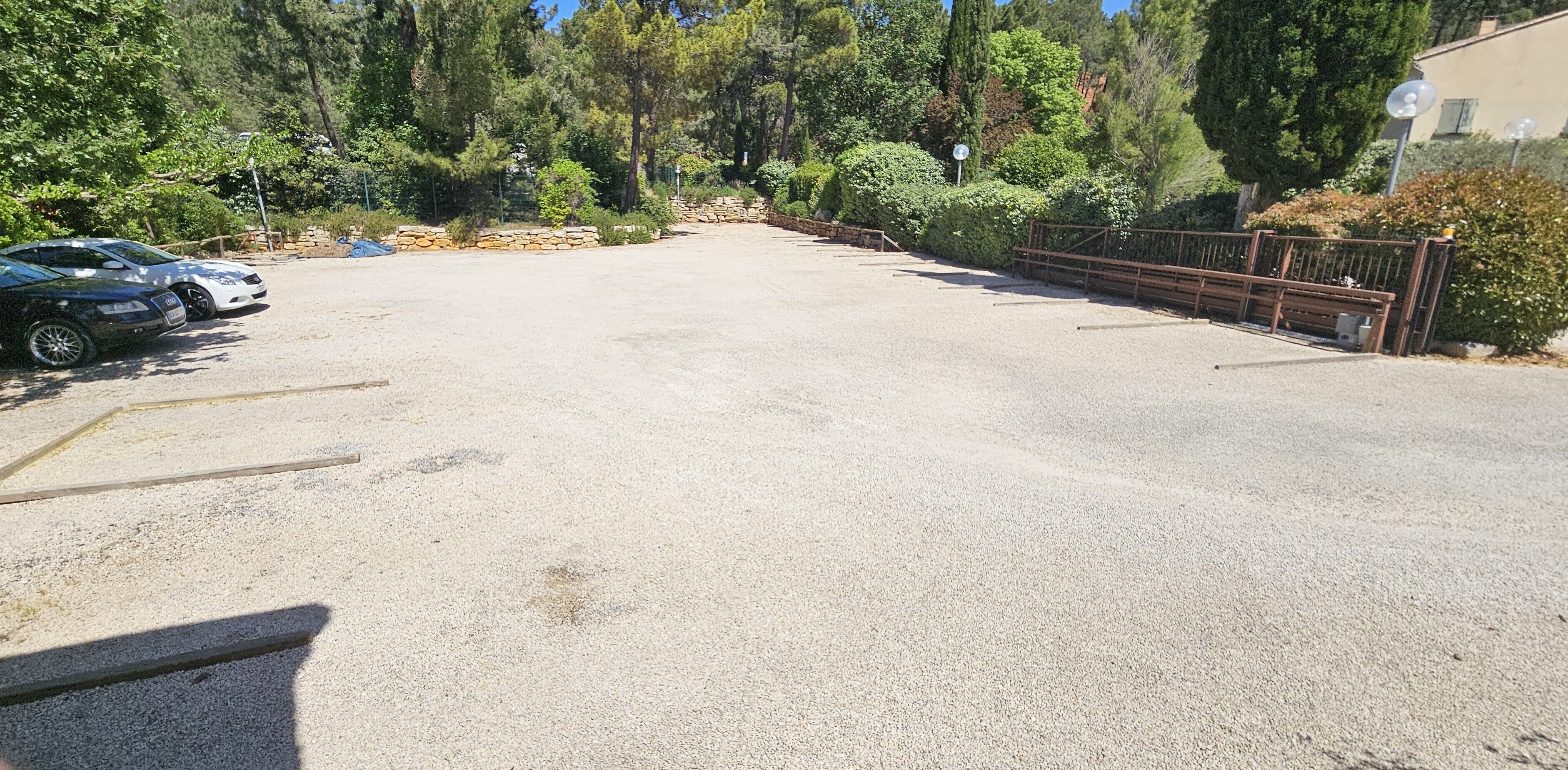 A gravel parking area with a few cars, surrounded by dense trees and a stone wall.