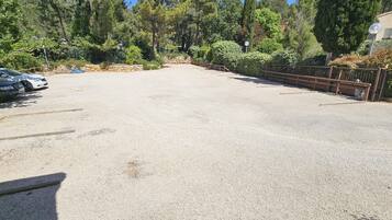A gravel parking area with a few cars, surrounded by dense trees and a stone wall.