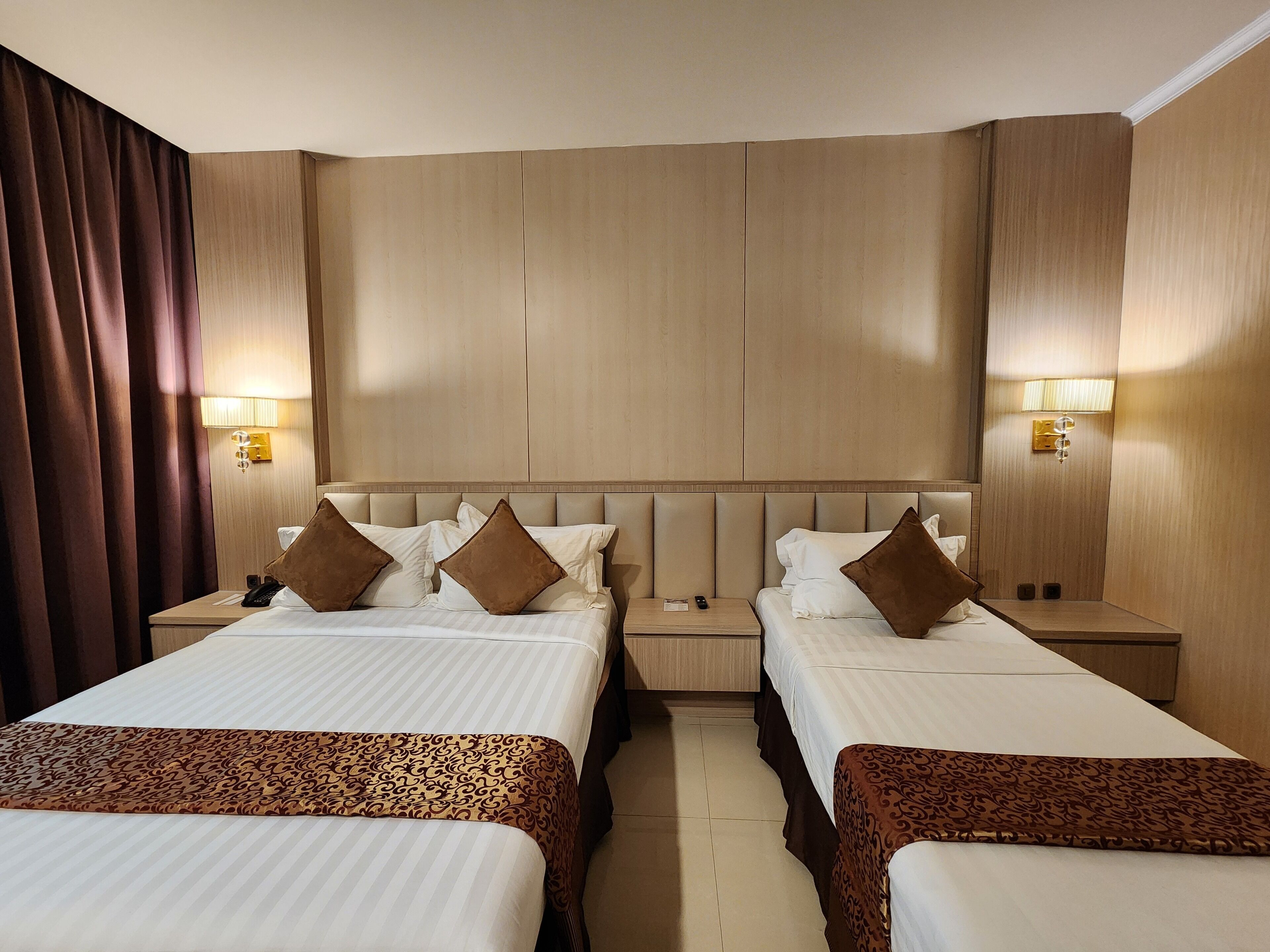 A hotel room with two beds, a headboard, bedside tables, lamps, and a curtain.