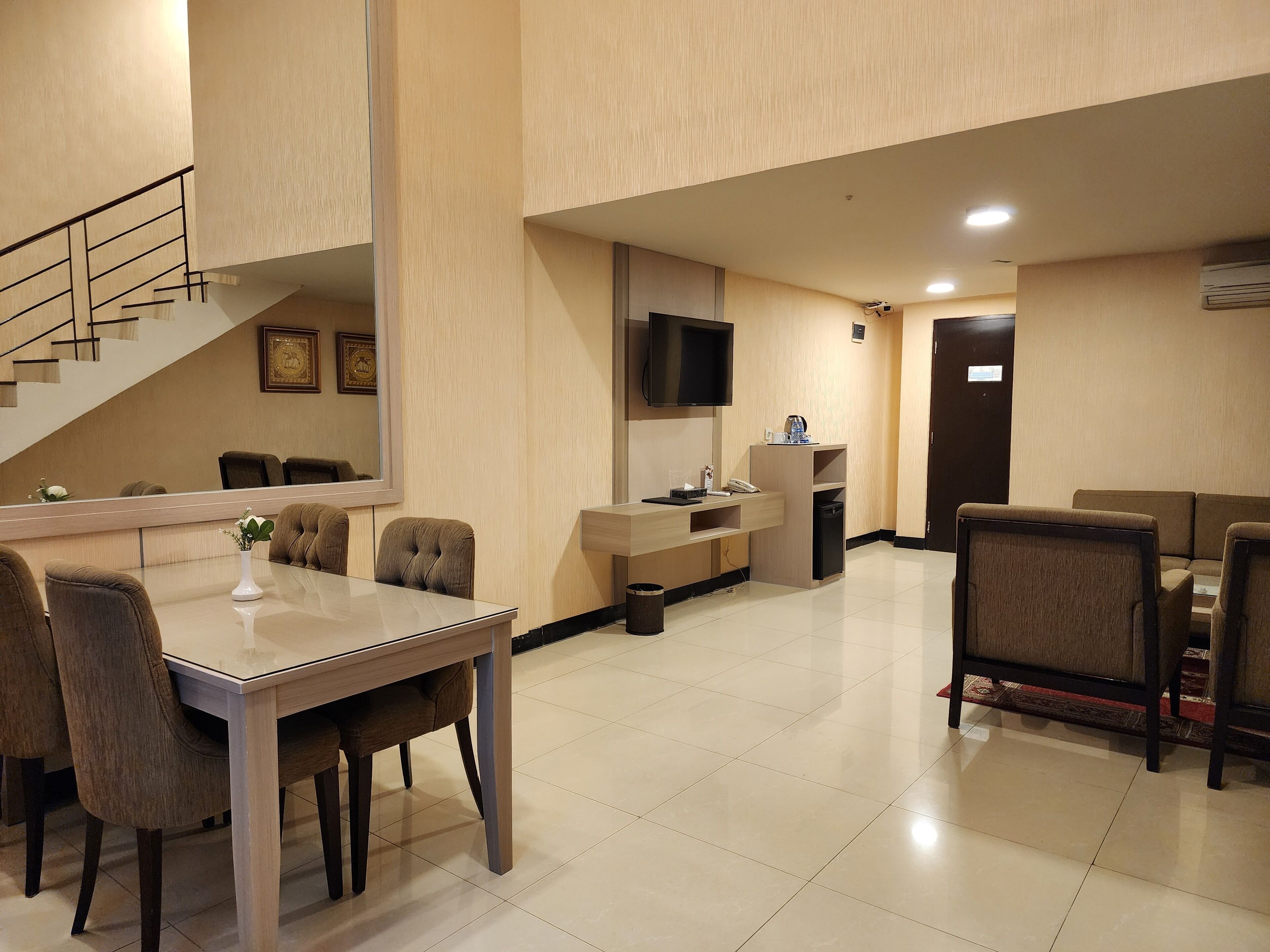 A hotel room with a dining area, a TV mounted on the wall, a staircase, and a door.
