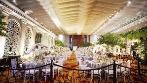 A grand hall with ornate ceiling, white floral arrangements, and a central aisle leading to a stage. - Grand Paragon (Jakarta)