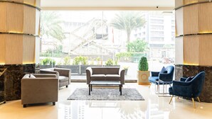 A lobby with a sofa, armchairs, a coffee table, and a view of a building with a staircase. - Grand Paragon (Jakarta)