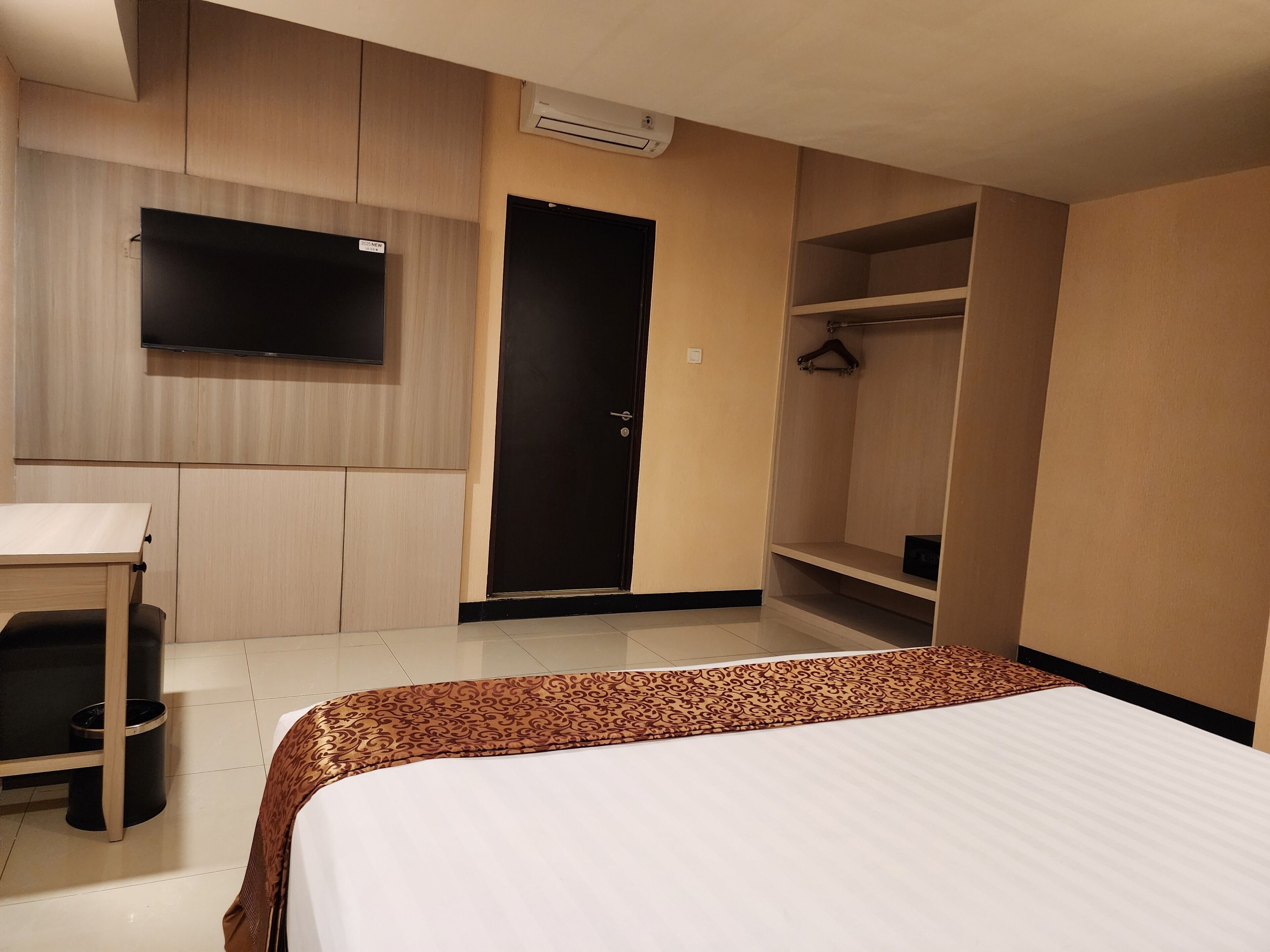 A hotel room with a bed, a desk, a wardrobe, a television, and a door.