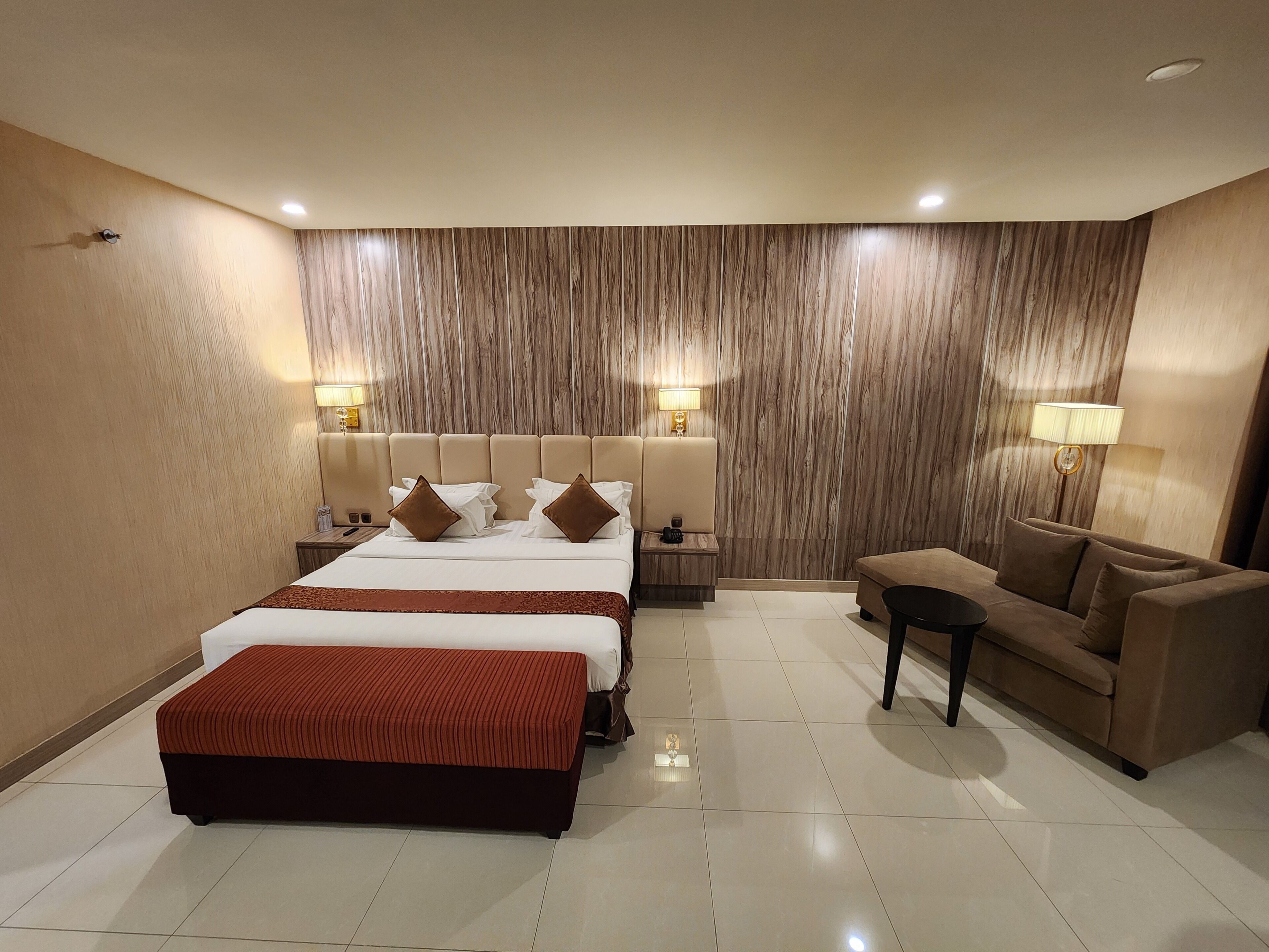 A hotel room with a large bed, a sofa, a small table, and two bedside lamps.