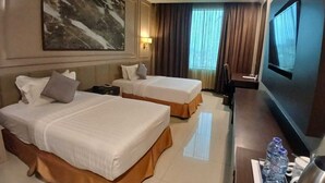 A hotel room with two beds, a TV, a desk with a lamp, and a large painting on the wall. - Grand Paragon (Jakarta)
