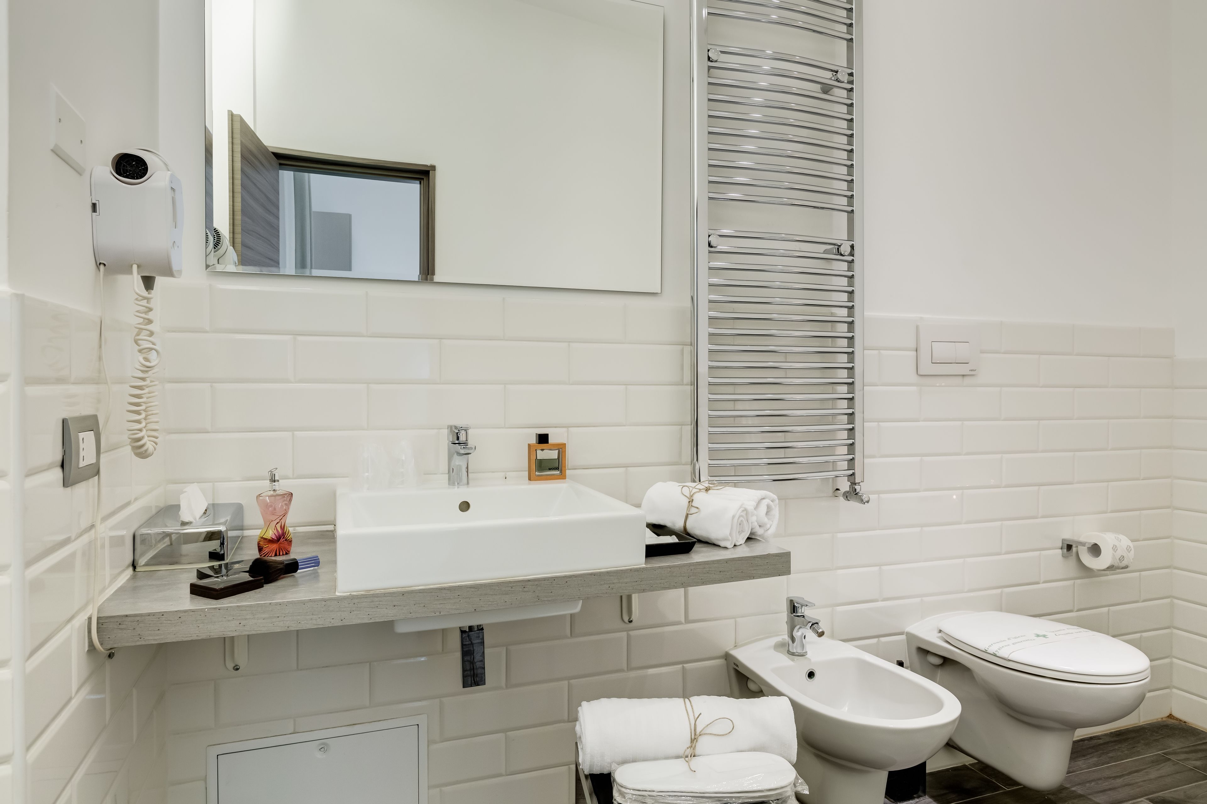 A modern bathroom with a white sink, a mirror, a towel rack, a bidet, and a toilet.