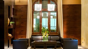 A modern lobby with a wooden wall, a glass window, a sofa, a table, and two armchairs. - Hotel Dubna Skala (Zilina)