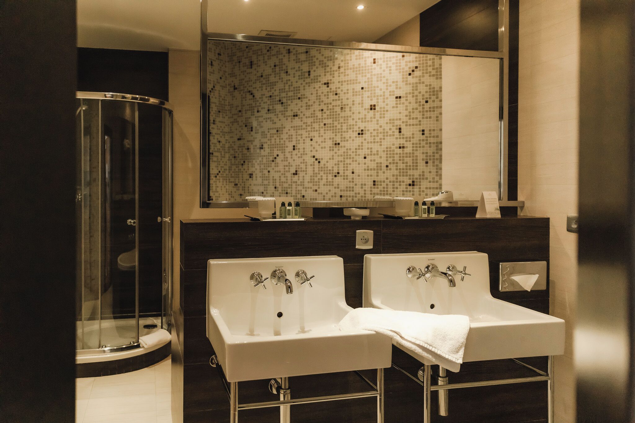A modern bathroom with a glass-enclosed shower, two sinks with faucets, and a tiled backsplash.