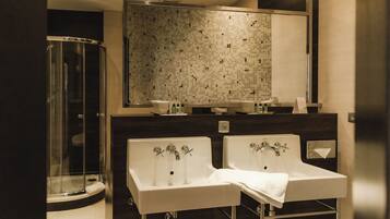 A modern bathroom with a glass-enclosed shower, two sinks with faucets, and a tiled backsplash.