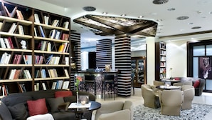 A modern library with bookshelves, a central seating area, and a bar. - Hotel Dubna Skala (Zilina)