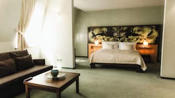 Habitación de hotel con cama, sofá, mesita de noche y un cuadro grande en la pared.