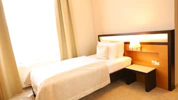 Ein Hotelzimmer mit Bett, Nachttisch, Lampe und einem Fenster mit Vorhängen.