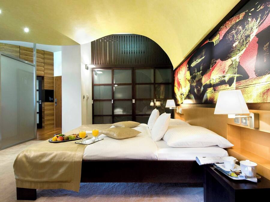 Quarto de hotel com uma cama, mesa de cabeceira e um quadro grande na parede.