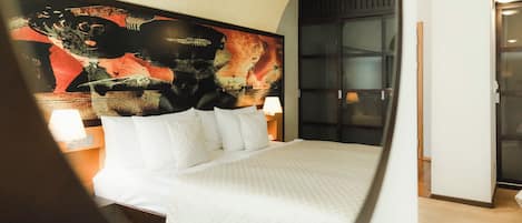 Una habitación de hotel con una cama grande, una mesita de noche con una lámpara y un cuadro abstracto de gran tamaño en la pared.
