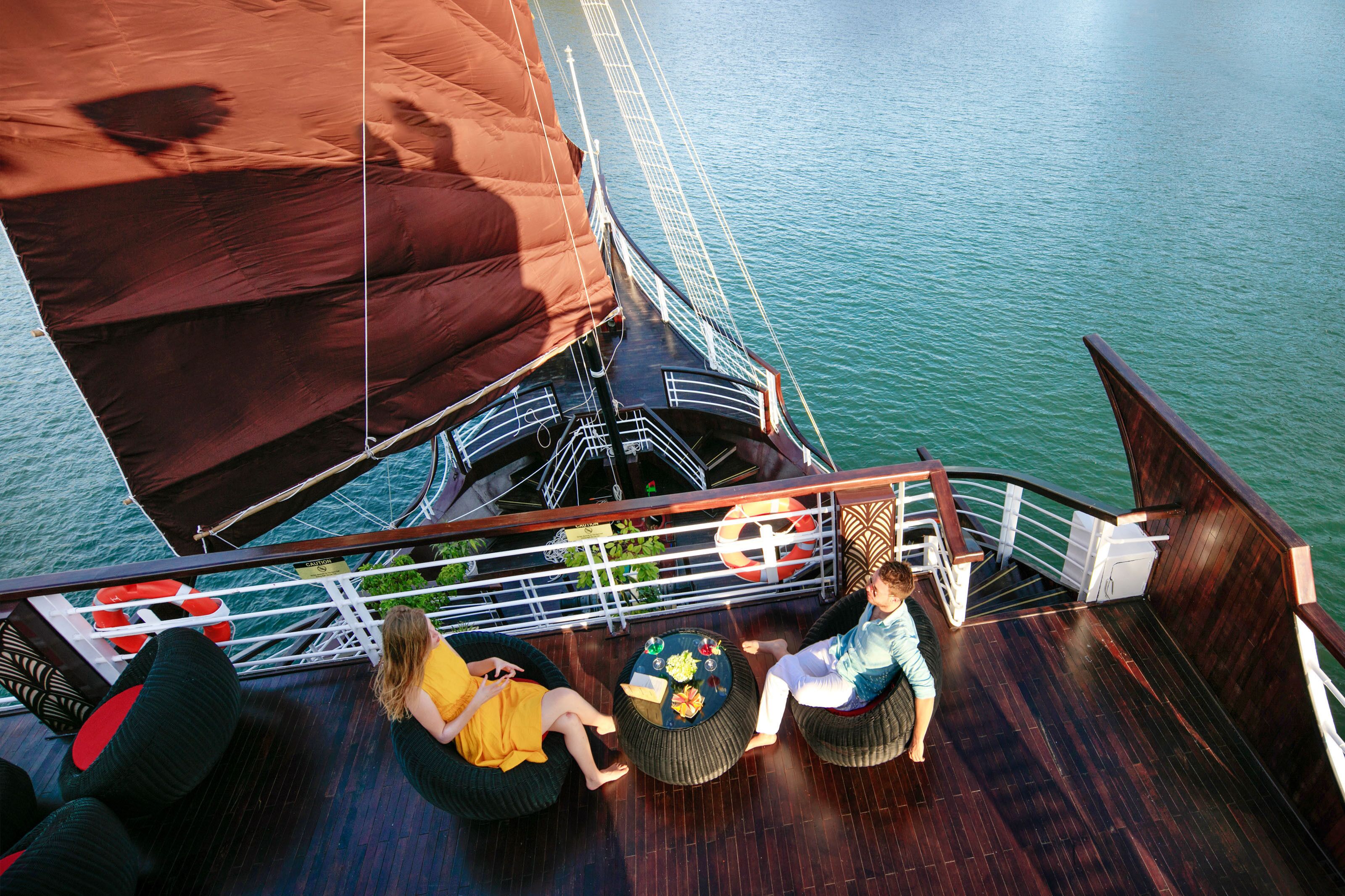 A deck with two round tables, a person in a yellow dress, and another in a blue shirt.