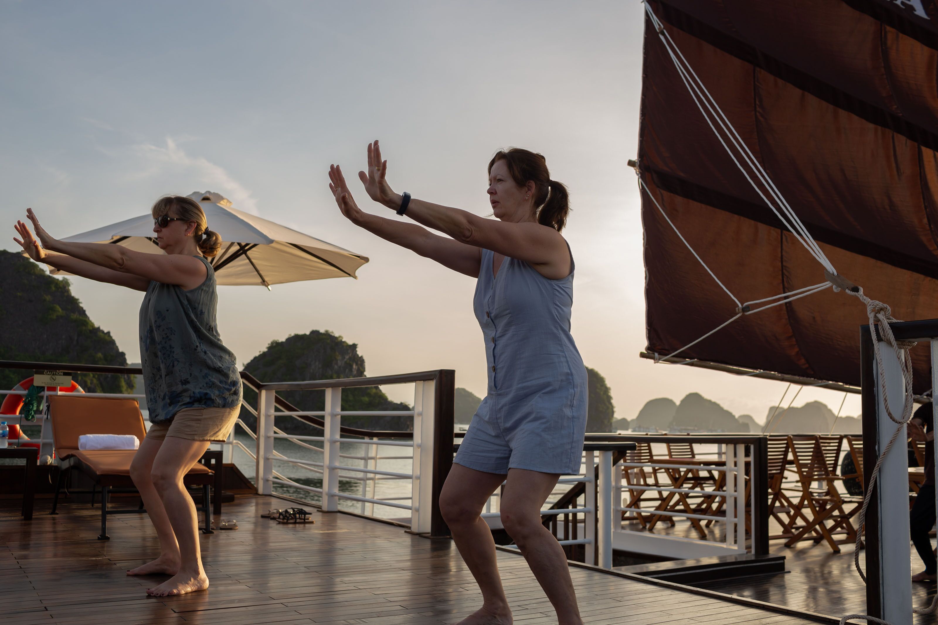 Two people performing a dance on a wooden deck with a railing and a view of the sea.
