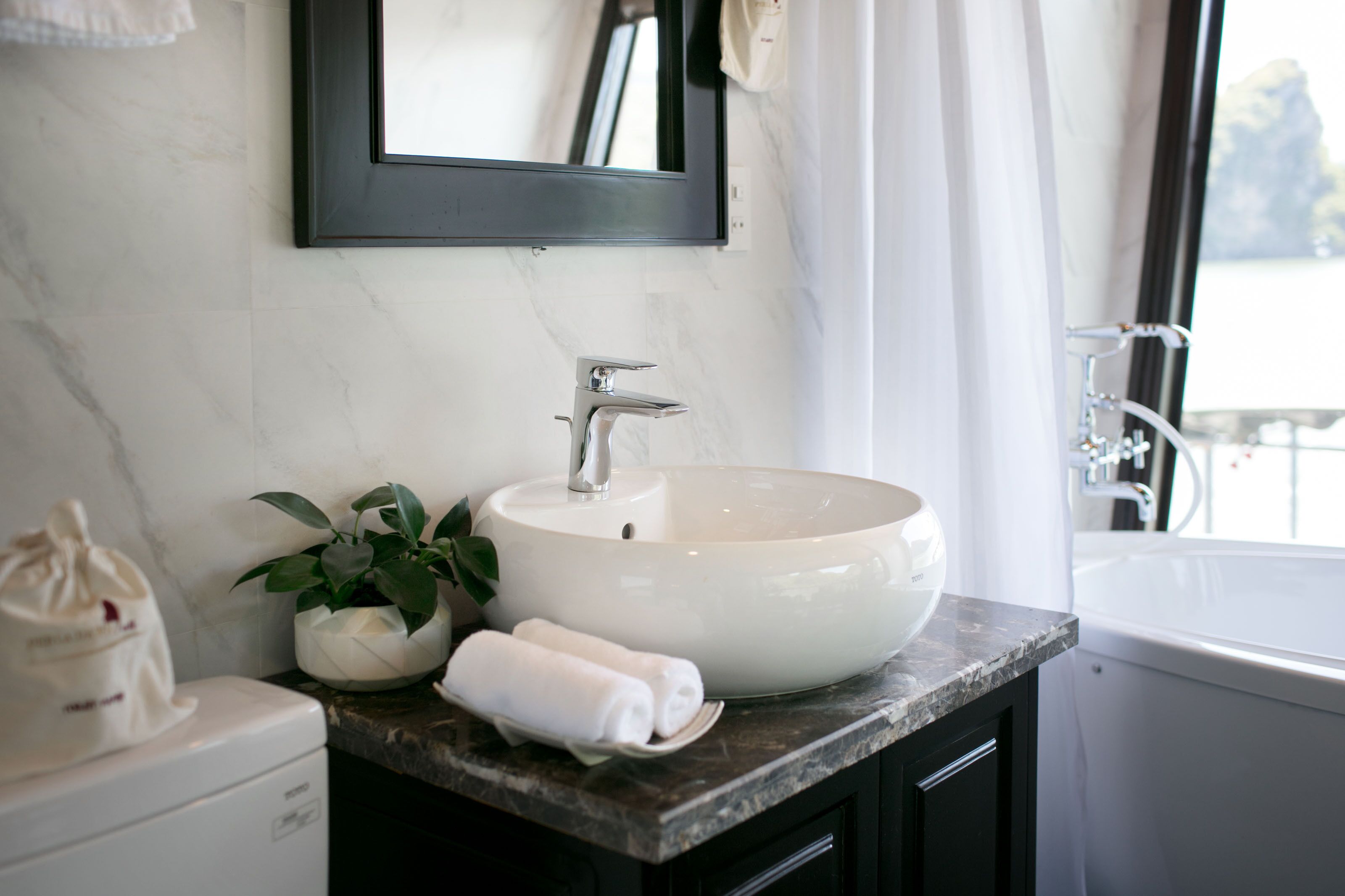 A bathroom with a white sink, a mirror, a potted plant, and a towel on the counter.