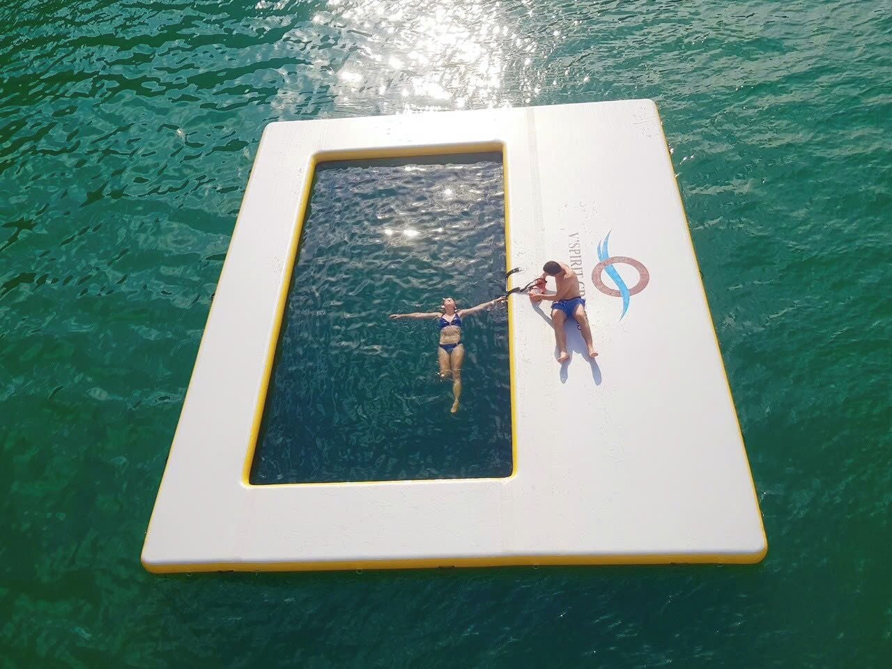 Une piscine rectangulaire bordée de jaune, dans laquelle une personne flotte.