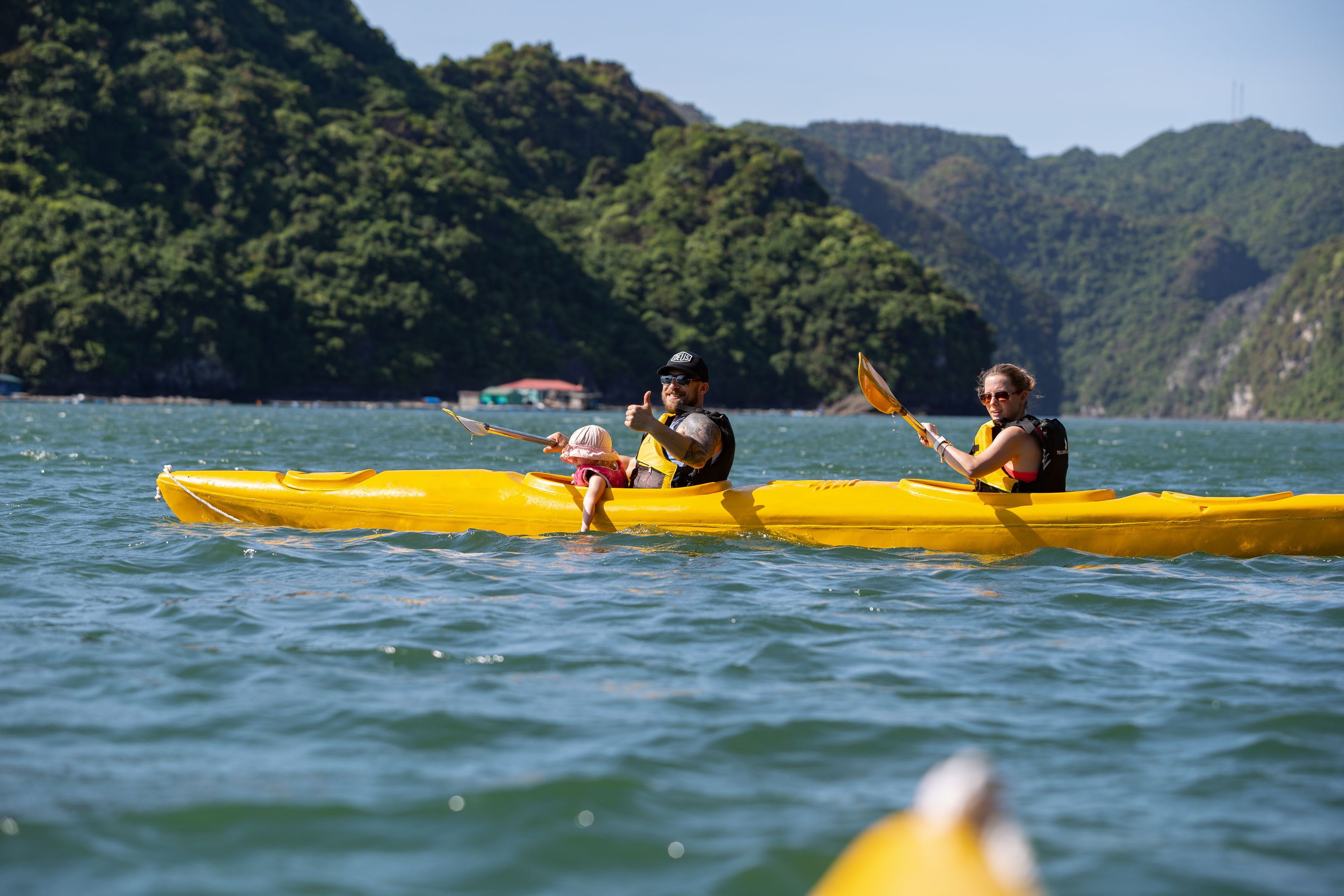 Dos personas en un kayak amarillo sobre un cuerpo de agua, con montañas al fondo.