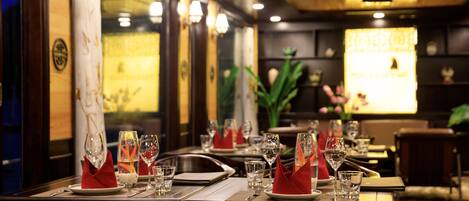 A restaurant interior with tables set for dining, featuring red napkins, clear glasses, and a warm ambient lighting.