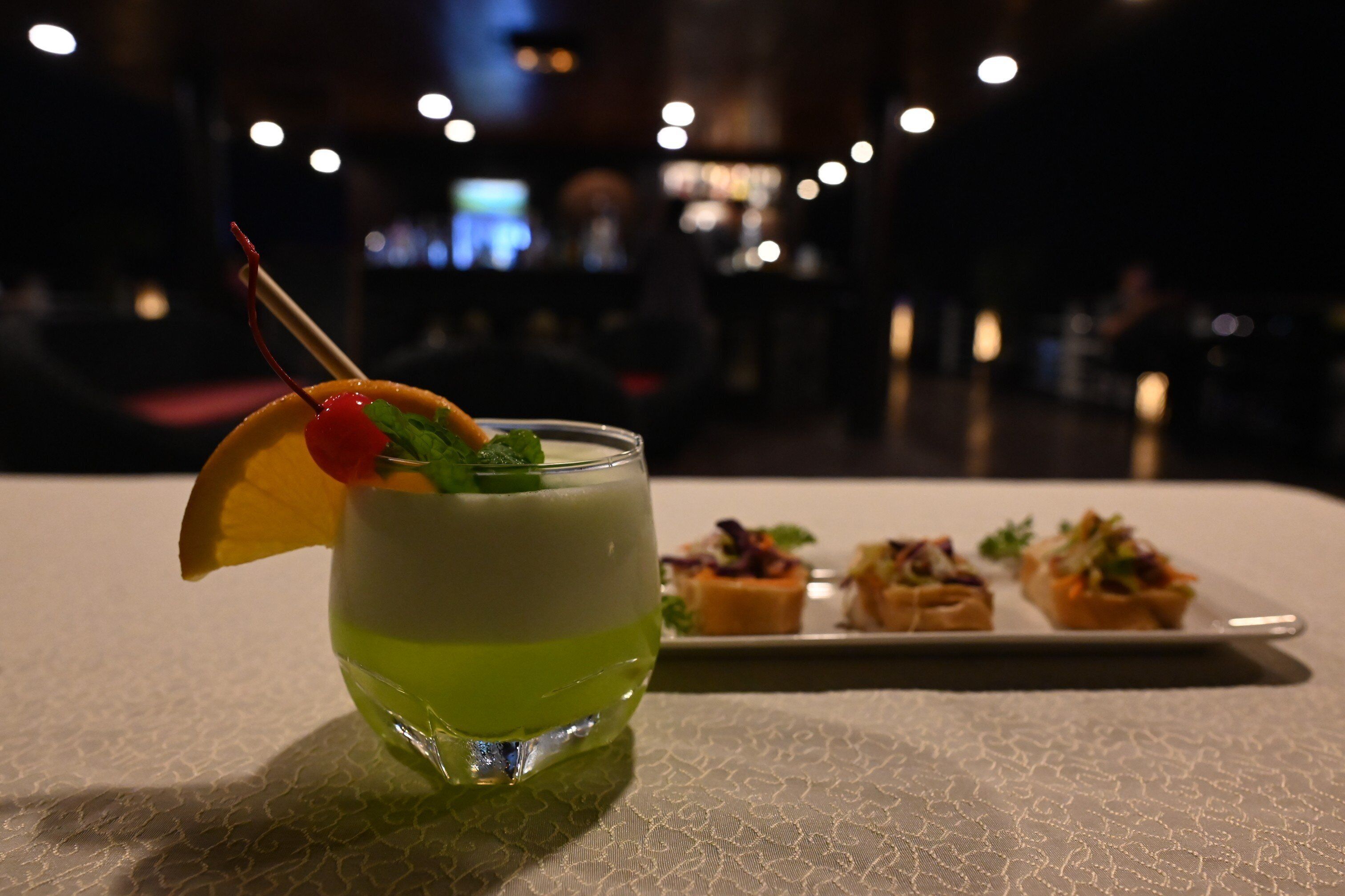 A cocktail glass with a cherry garnish and mint leaves on a table with a lace tablecloth.
