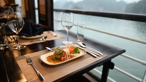 A dining table with a plate of food, a fork, a knife, and two wine glasses. - V'Spirit Cruises (Tuan Chau)