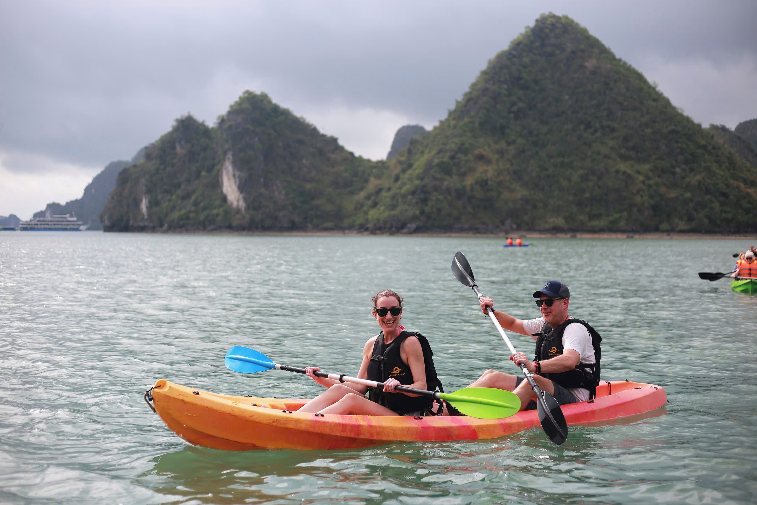 Dos personas kayakando sobre aguas tranquilas, con un paisaje montañoso al fondo.