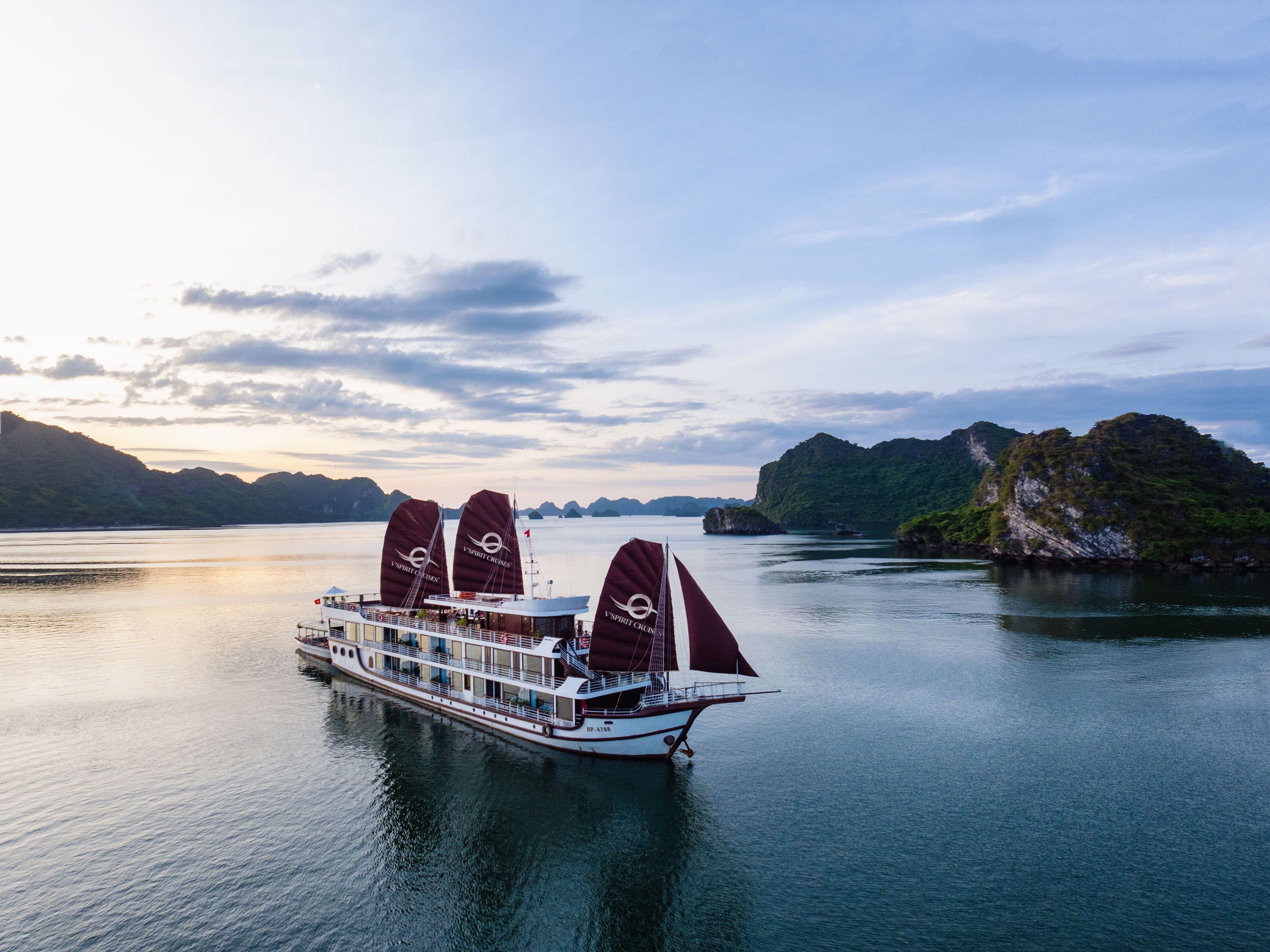 A river cruise ship with multiple decks and a flag, sailing on calm waters with mountainous terrain in the background.