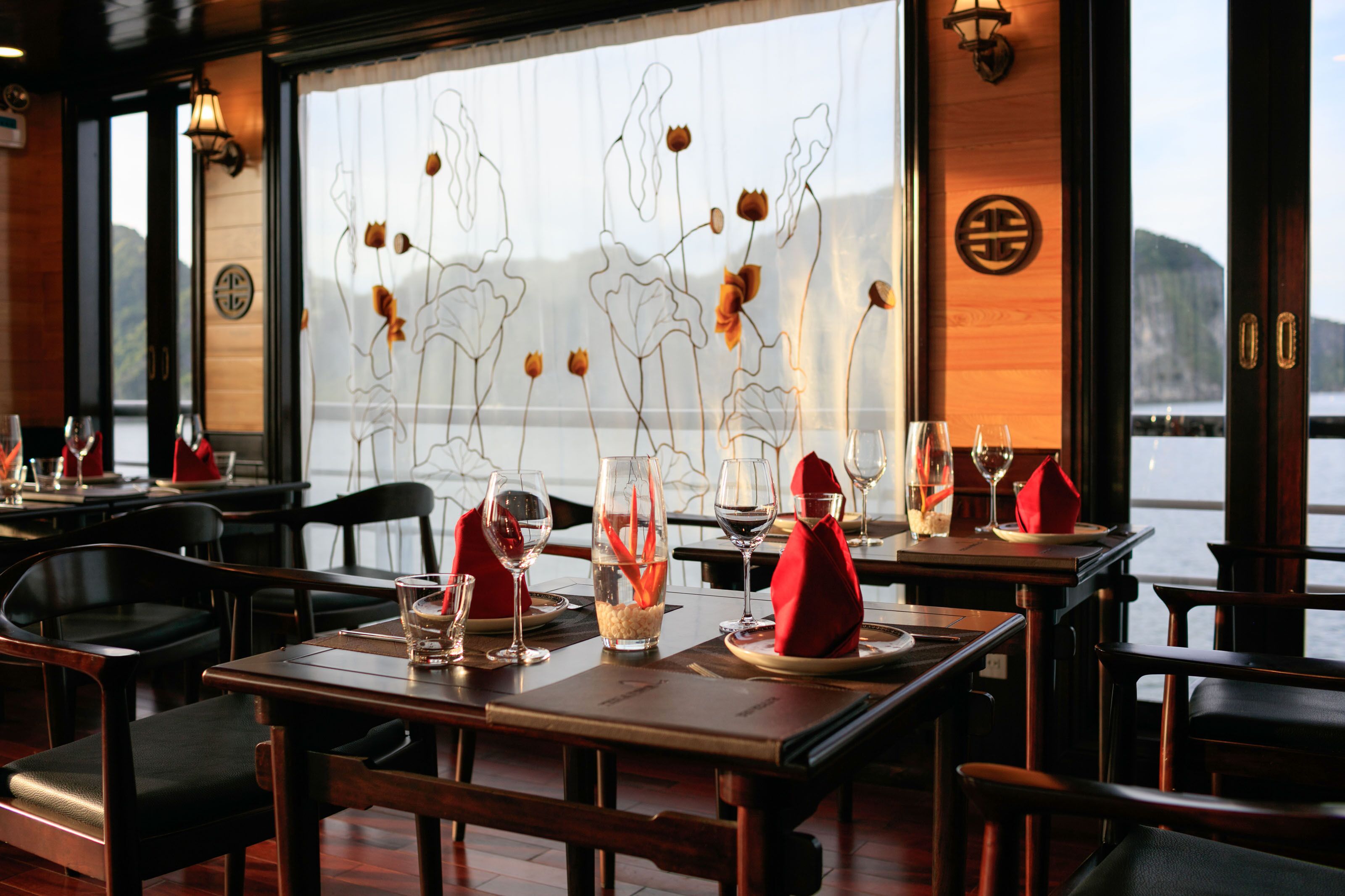 A restaurant with tables set for dining, a view of the sea through large windows, and decorative wall art.