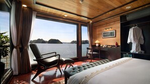 A bedroom with a large bed, a desk, and a chair, overlooking a body of water. - V'Spirit Cruises (Tuan Chau)