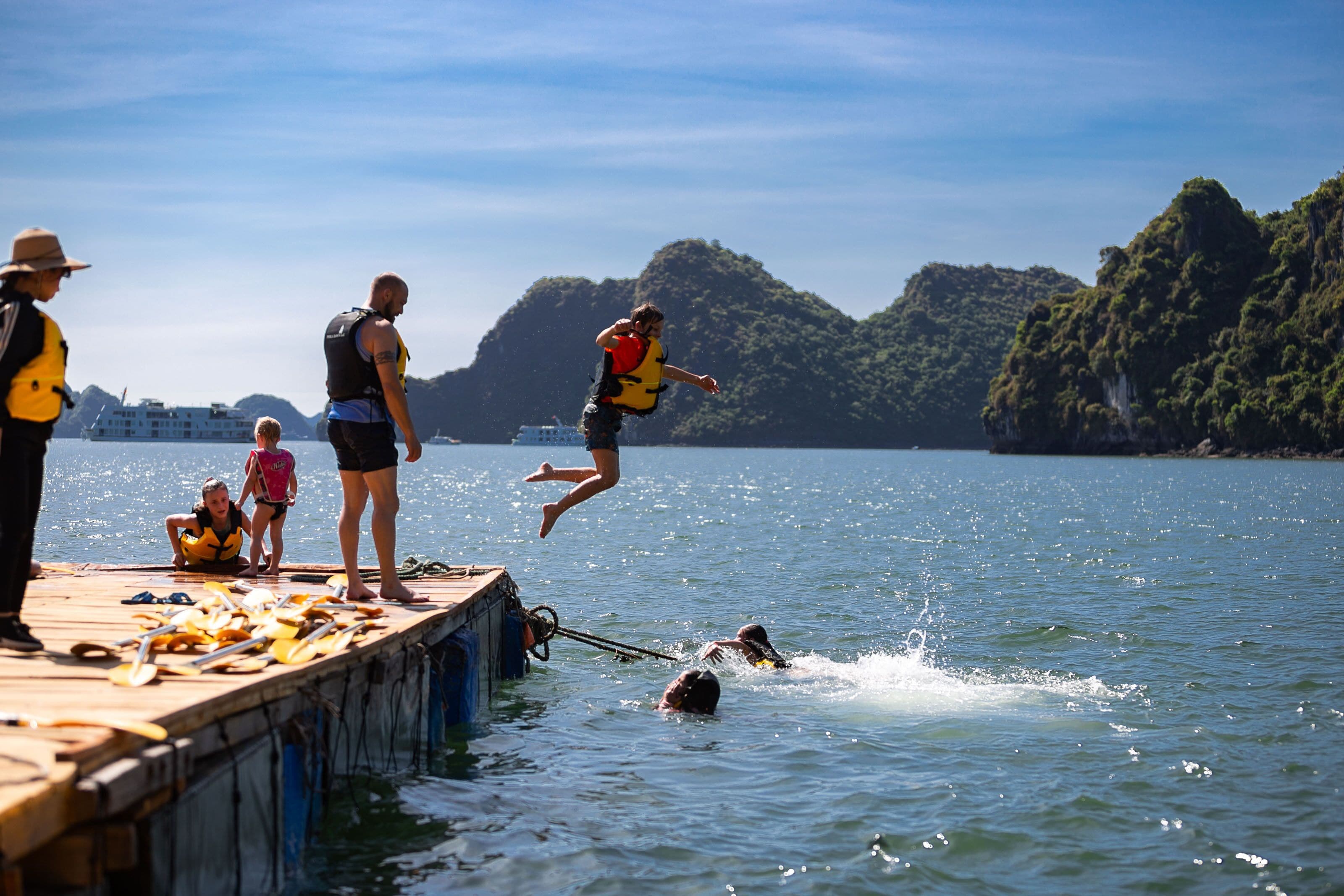 A dock with people preparing for water activities, a boat in the background, and a mountainous landscape.