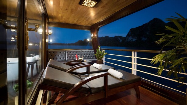 A balcony with wooden flooring, cushioned chairs, a table, and a potted plant. - V'Spirit Cruises (Tuan Chau)