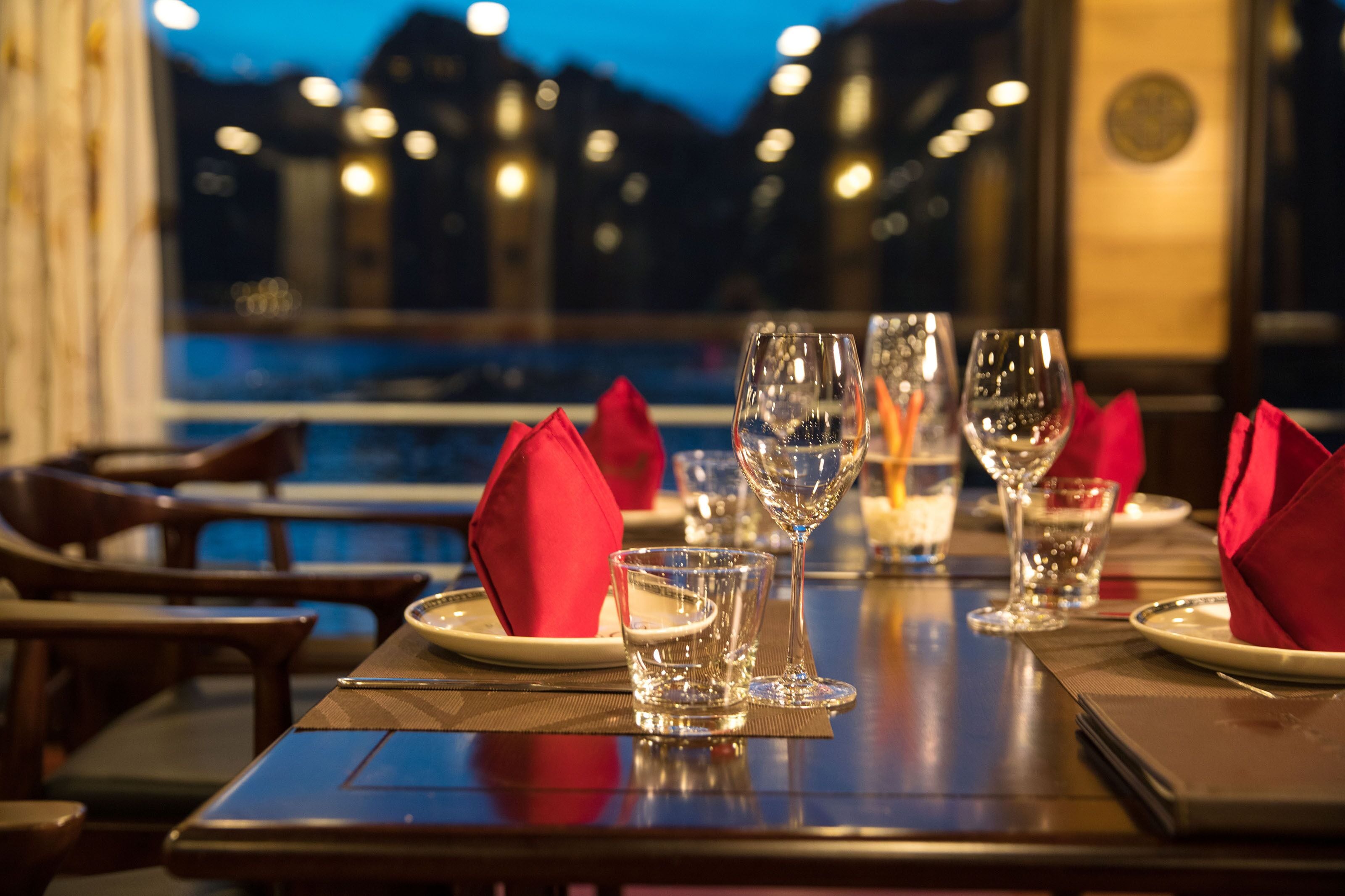 A dining table set with red napkins, clear glasses, and a candle.