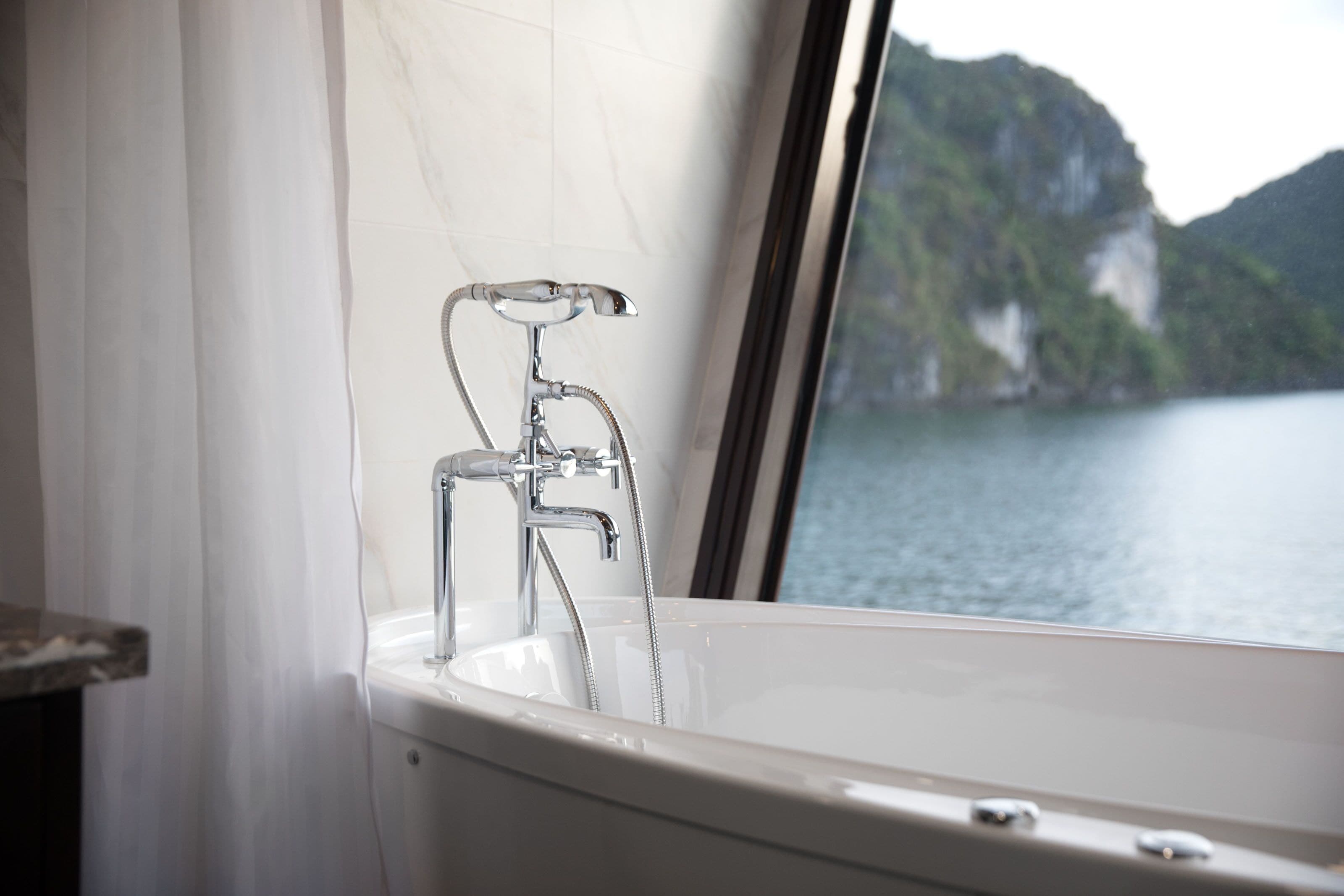 A bathroom with a bathtub, a shower, and a window with a view of a body of water and mountains.