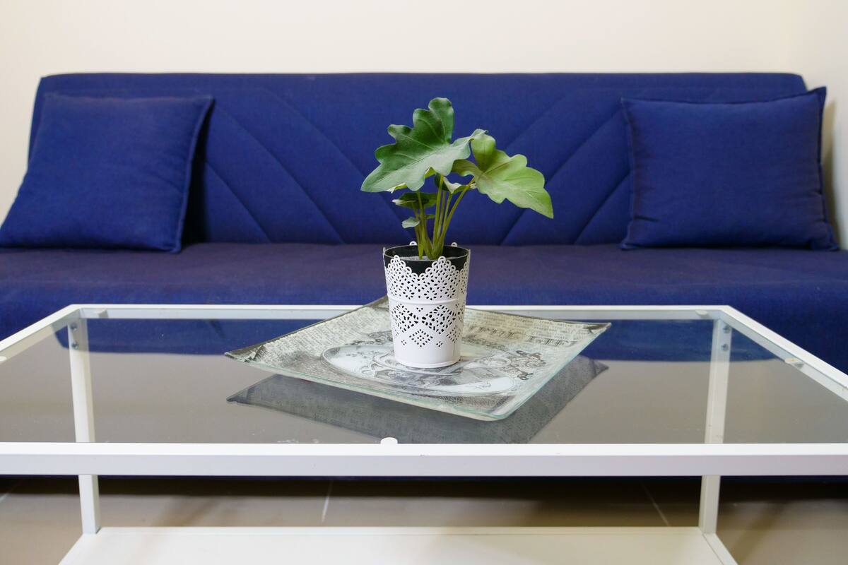 Ein Glastisch mit einer dekorativen weißen Vase, die eine Pflanze enthält, auf einer Tischdecke mit Muster.